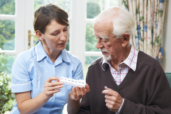 Image of a home health nurse helping a senior man with his pill box