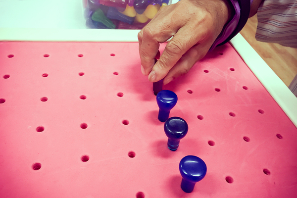 Image of a mature adult's hands completing an occupational therapy exercise known as pegs
